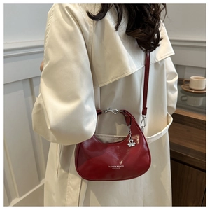Detail of red crescent shoulder bag with glossy finish and clover charm on a model