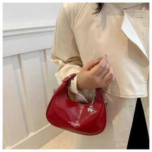 Detail of red crescent hobo bag with gold clover pendant and minimalist leather texture