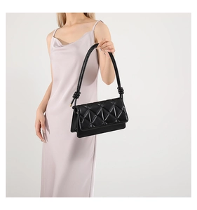 Detail of black quilted faux leather shoulder bag featuring decorative knotted straps