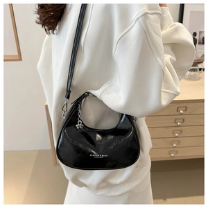 Detail of black patent leather hobo bag with fashion logo and metal butterfly charm