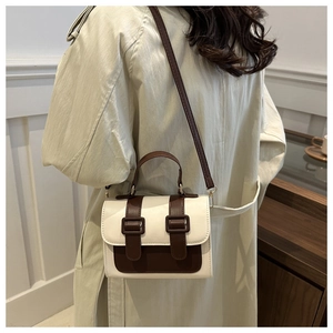 Detail view of a vintage contrast shoulder bag styled with a tan coat in a warm room