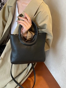 Minimalist black pebble leather handbag with circular handle and detachable shoulder strap