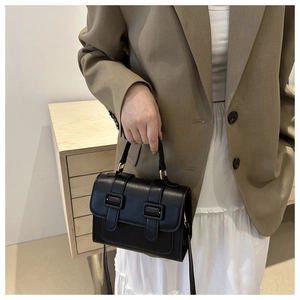 Detail of a vintage black leather crossbody bag held by a model with khaki suit