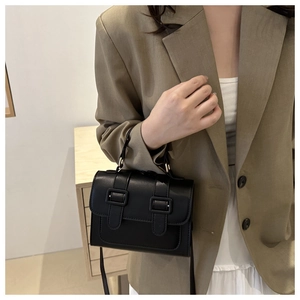 Close-up of a minimalist black leather crossbody bag with top handle and strap detailing