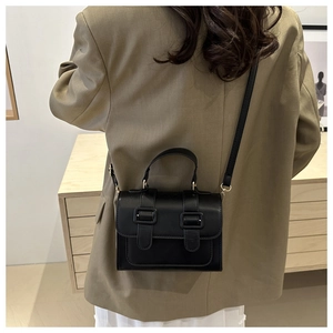 Classic black leather crossbody bag with dual buckles shown on a model in beige suit