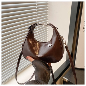 Detailed view of dark brown crescent bag with glossy finish and clover charm detail