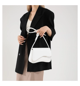 Bolso bandolera blanco elegante con borde ondulado único sobre una chaqueta blazer negra