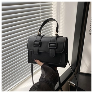 Close-up of black leather crossbody bag with dual buckles and elegant shadow lighting