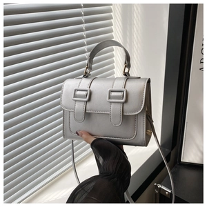 Detail shot of a silver metallic crossbody bag with double buckle flap and top handle