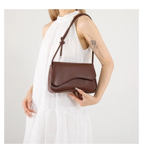 Detalle de un bolso bandolera de cuero marrón oscuro con solapa curva y nudos decorativos