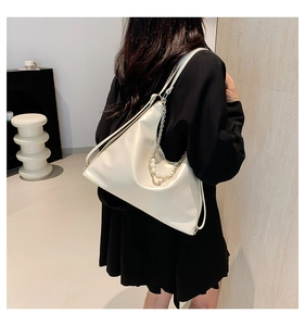 Detail view of cream white tote bag with elegant pearl and metal chain decoration