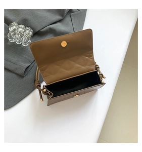 Detail view of brown leather bag with golden magnetic clasp and twisted handle design