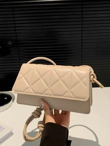Beige quilted shoulder bag with knotted strap and gold hardware held in hand