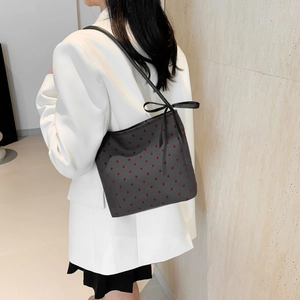 Borsa a spalla con cuori rossi e fiocco nero indossata da una modella in bianco