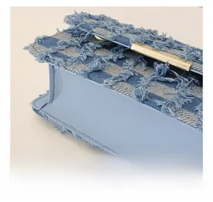 Detail of denim checkered pattern with fringe edges and golden metal buckle on fashion bag