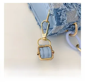 Detailed close-up of blue denim cross-body bag featuring fringe edges and golden hardware