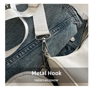 Detail von silbernem Metallkarabiner und weißem Stoffgurt an einer Canvas-Tasche