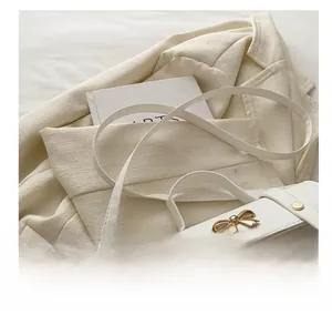 Close-up of a white fashion bag featuring a golden bow buckle and smooth faux leather texture