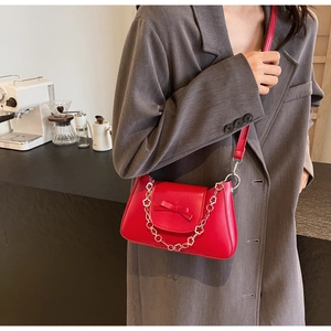 Sac rouge avec nœud et chaîne florale en métal porté sur un blazer gris élégant