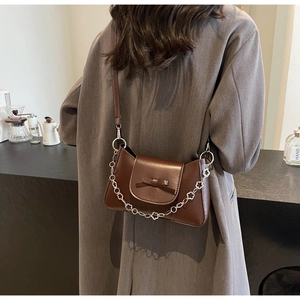Détail d'un sac bandoulière marron foncé avec nœud et chaîne métallique à fleurs argent