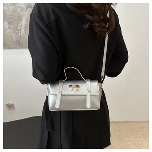 Modern silver rectangle crossbody bag with golden bow clasp shown on a model's back