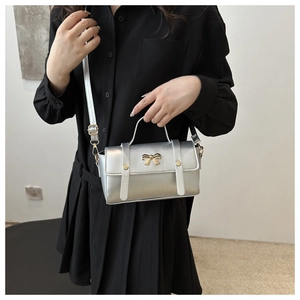 Detail of silver mini crossbody bag with glossy metallic finish and golden bow decoration