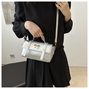 Detail view of silver crossbody bag with golden bow ornament on a black pleated skirt