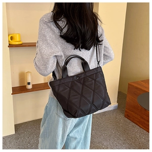 Detail of black quilted nylon bucket bag with dual handles and metal buckle accents