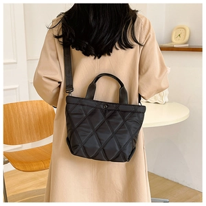 Model showing black quilted nylon bucket bag with large diamond stitching and long strap