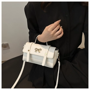 Detail of white leather handbag featuring golden bow buckle and adjustable strap