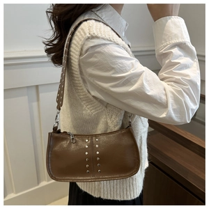 Détail du sac sous le bras en cuir marron foncé avec rivets argentés sur la bandoulière