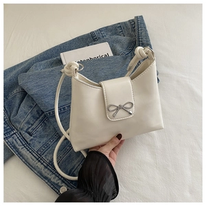 Detail of creamy white crossbody bag with silver bow ornament and leather knot shoulder strap