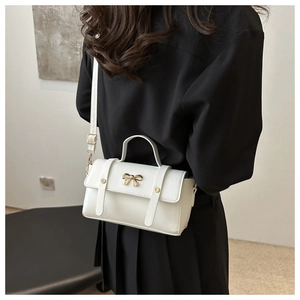 Detailed view of a white leather crossbody bag with golden bow and rivet accents