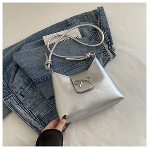Close-up of silver shoulder bag with metallic bow detail on denim jacket background