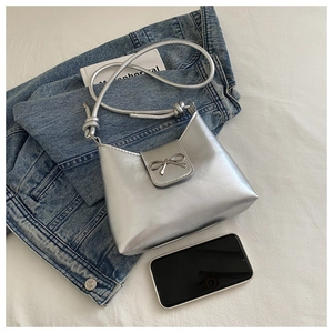 Detailed view of silver metallic shoulder bag with metal bow and knotted strap design