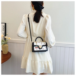 Detail van witte crossbodytas met kersenprint, metalen slot en geweven handvat