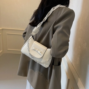 Sac à épaule en cuir blanc crème avec rabat à nœud et chaîne fleurie sur fond neutre