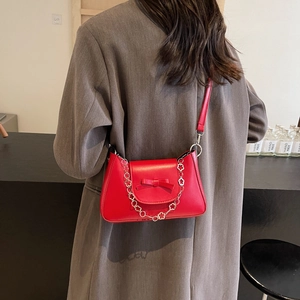 Sac bandoulière rouge élégant avec nœud et chaîne fleurie sur une veste de blazer grise