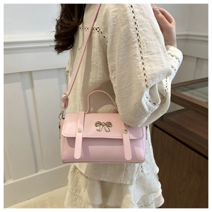 Detailed view of a pink PU leather handbag with golden bow metal and shoulder strap