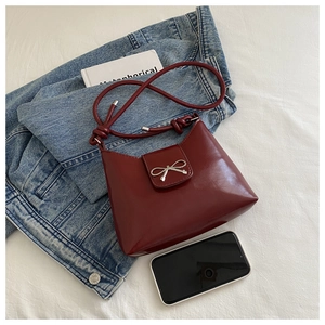 Detail of burgundy glossy handbag with silver metal bow and slim knotted strap