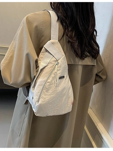 Sac bandoulière minimaliste en nylon beige pour femme porté avec un trench décontracté