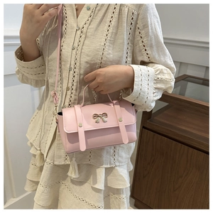 Detailed view of pink PU leather handbag featuring a golden metal bow and rivet details