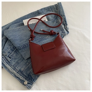 Close-up of a burgundy leather crescent bag with knot strap detail on denim background