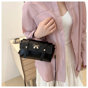Detail of a black leather handbag with a golden bow buckle worn with a pink shirt