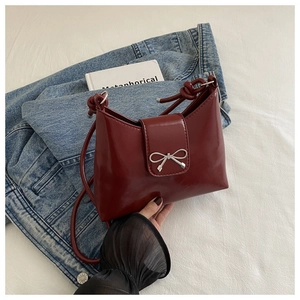 Close-up of wine red patent leather shoulder bag featuring a silver bow and knotted strap