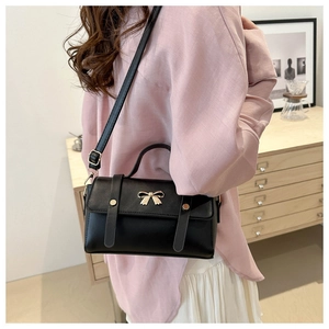 Detail of a chic black square bag with golden bow hardware worn by a model in a cozy room