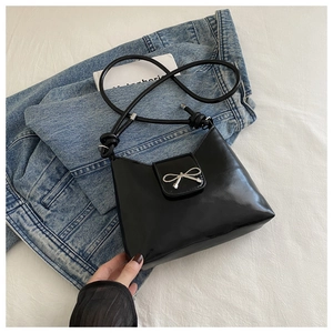 Detail of black faux leather shoulder bag with silver bow buckle on blue denim jacket