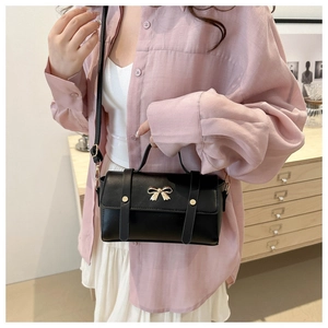 Detail of black crossbody bag with gold bow clasp and rivet straps on a pink shirt