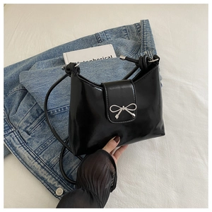 Detailed close-up of a black glossy shoulder bag with a silver metal bow decoration