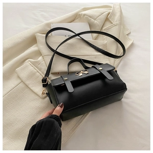 Detail of black leather handbag featuring a golden metal bow and adjustable shoulder strap
